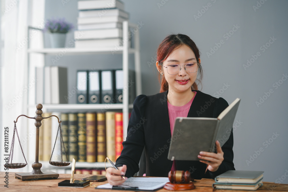 Professional female lawyer at her desk with legal books and scales, reading and taking notes in an office setting.