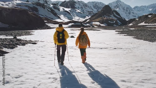 Young couple of tourists with backpacks and hiking poles walks in sunset snowy mountains. Active lifestyle video