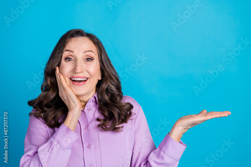 Photo of adorable lovely woman wear violet shirt holding empty space isolated blue color background