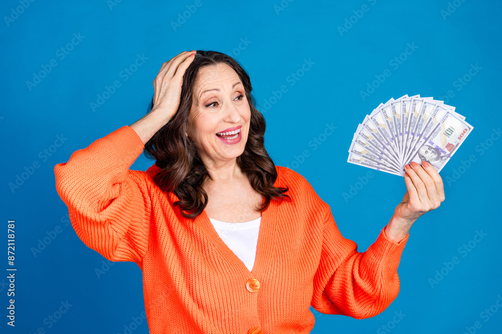 Photo portrait of attractive senior woman hold money fan look amazed dressed stylish orange clothes isolated on blue color background