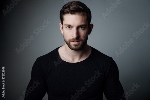 Handsome Young Man in Black Sweater Staring Intently at Camera with an Emotional, Anxious, and Skeptical Expression Against Gray Background