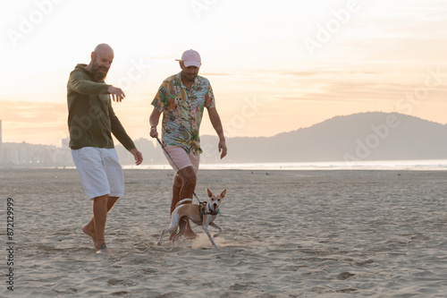 couple of homosexual men playing with their dog on the beach at sunrise