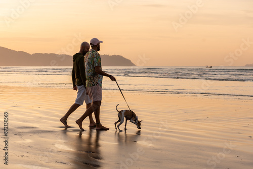 silhouette of a gay couple walking their dog on the beach at sunrise