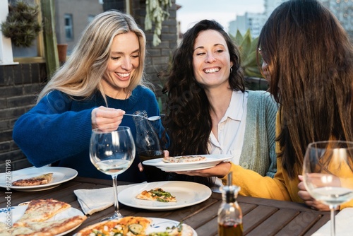 Young friends eating pizza and wine food at restaurant pizzeria outdoor. Happy women having fun enjoying dinner party together