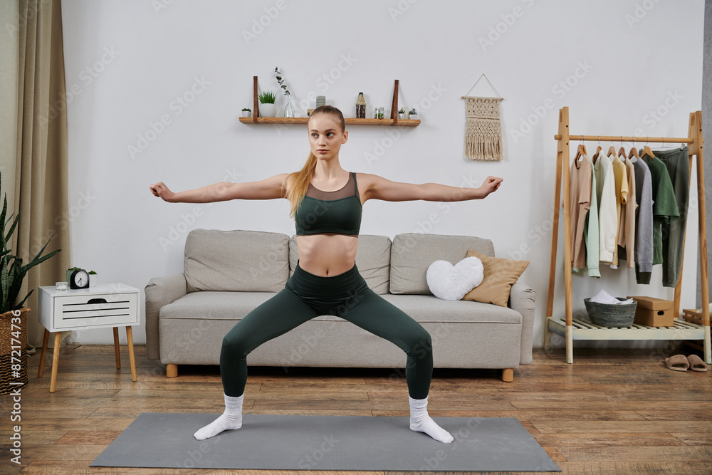 Obraz premium A young woman in a green sports bra and leggings performs a yoga pose in her living room.