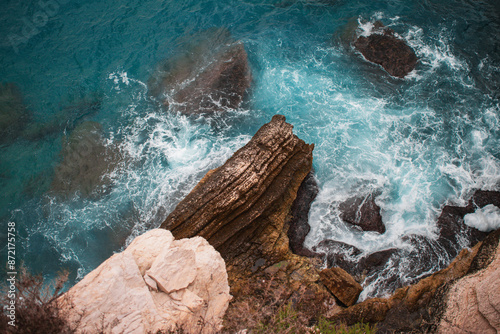 Helicopterview of cliff and rocks at the coast of the sea with rough waves and azure blue water photo