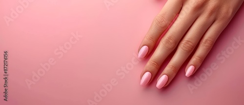  A woman's hand with a pink manicure against a pink backdrop, adorned with a ring atop it