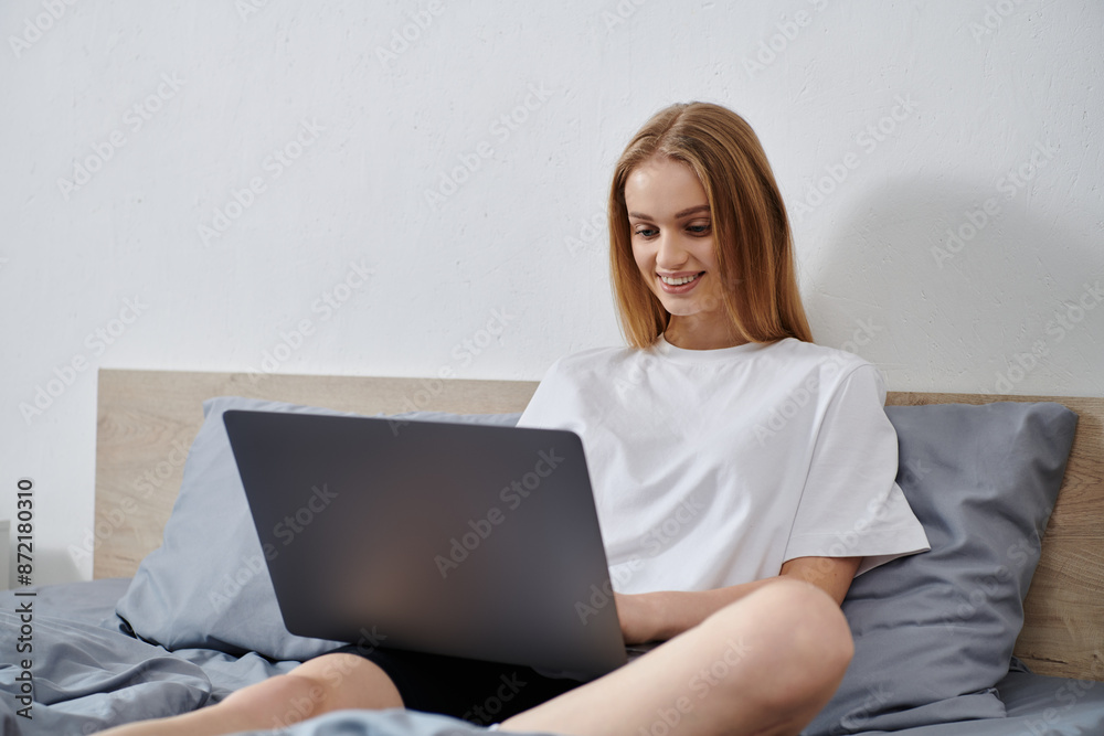 A woman uses a laptop while lying in bed. A woman uses a laptop while lying in bed.