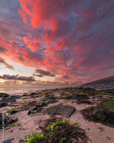 Spectacular red clouds above the exposed Wadden Sea. The setting sun creates a beautiful red glow in the damp clouds. It is low tide in the Wadden Sea, revealing the seaweed-covered stones. photo