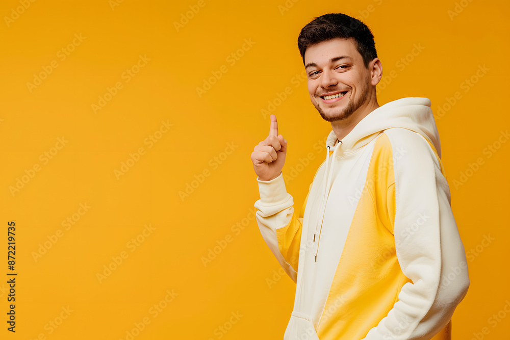 Side view young smiling happy man wear hoody casual clothes point thumb finger aside on area mockup workspace look camera isolated on plain yellow orange background studio portrait. Lifestyle concept Side view young smiling happy man wear hoody casual clothes point thumb finger aside on area mockup workspace look camera isolated on plain yellow orange background studio portrait. Lifestyle concept