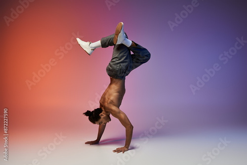 A young African American man performs a handstand while dancing against a gradient backdrop of red and purple.