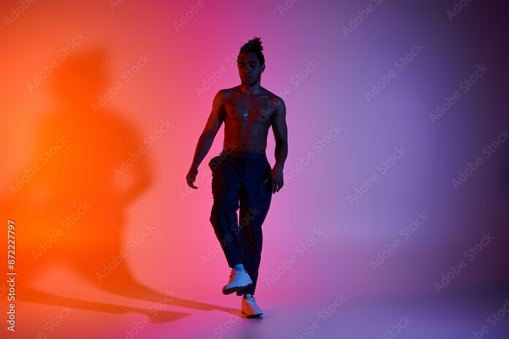 A young African American man dances on a pink and orange gradient background. He is wearing black pants and white shoes. A young African American man dances on a pink and orange gradient background. He is wearing black pants and white shoes.