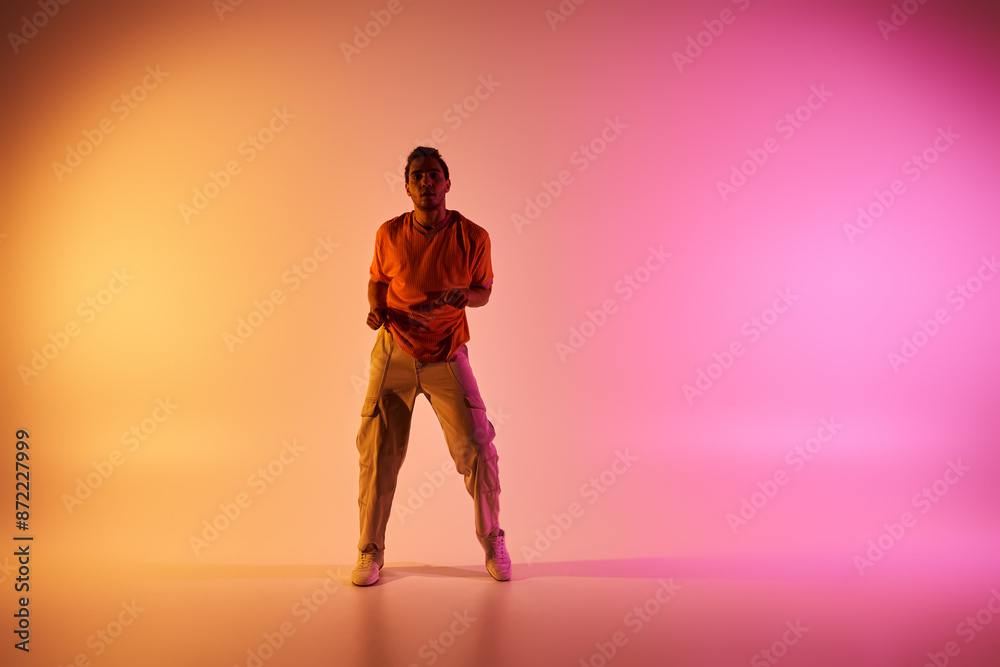 A young African American man dances against a vibrant gradient background. A young African American man dances against a vibrant gradient background.