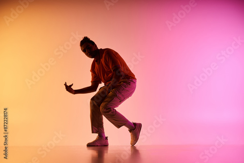 A young African American male dancer performs a move on a colorful gradient background.