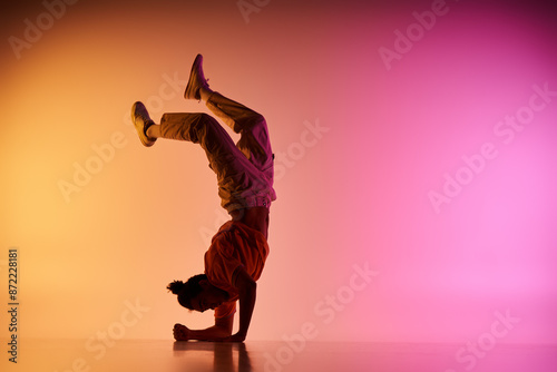 Fotografie A young African American man dances in a handstand against a vibrant pink and yellow gradient background