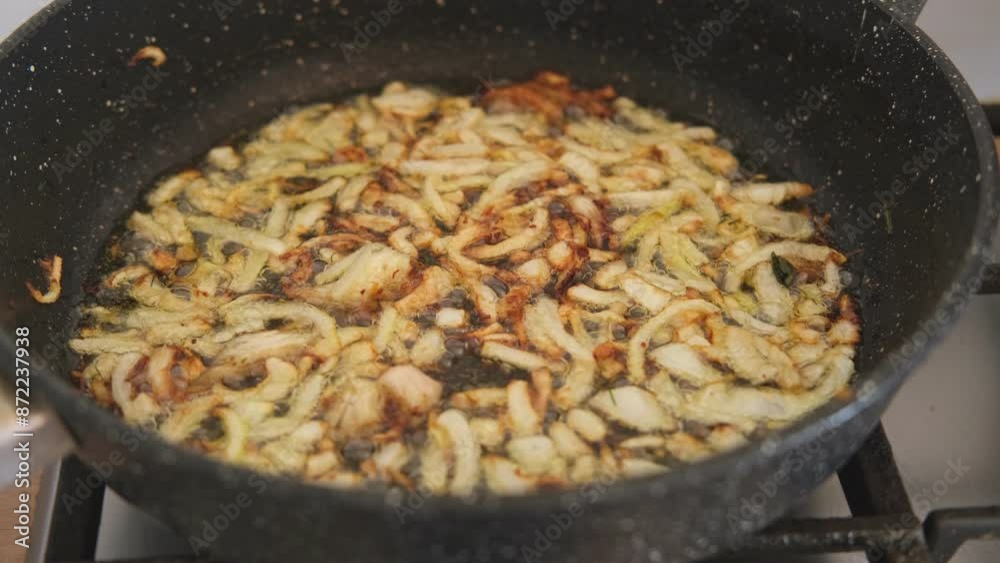 Crispy Fried Onion Bits with oil in the pan. Deep fried onion. Homemade frying onion in a black skillet on the gas oven. Top view. Golden sauteed onions. 4K Close up. Preparing dinner. Cooking at home