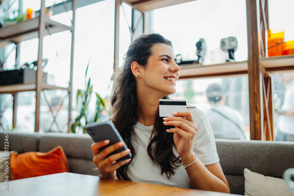 One young beautiful caucasian woman is buying online paying with credit card on mobile phone in cafe during the day