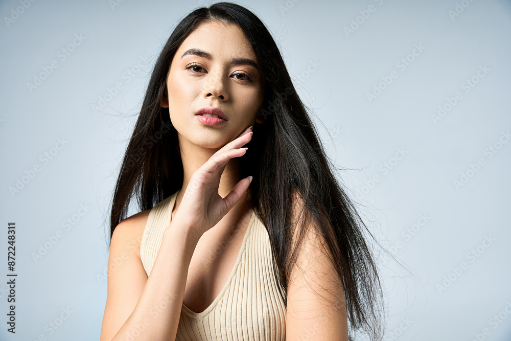 A young woman with long black hair poses confidently, wearing a stylish beige top. A young woman with long black hair poses confidently, wearing a stylish beige top.