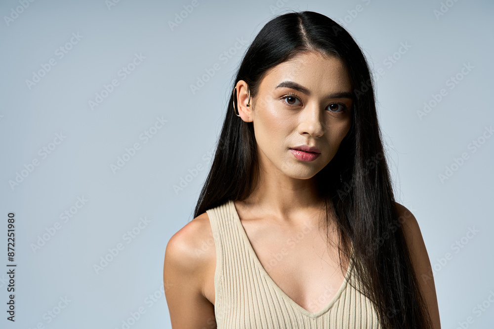Confident young woman with long black hair in beige tank top posed against light gray background. Confident young woman with long black hair in beige tank top posed against light gray background.