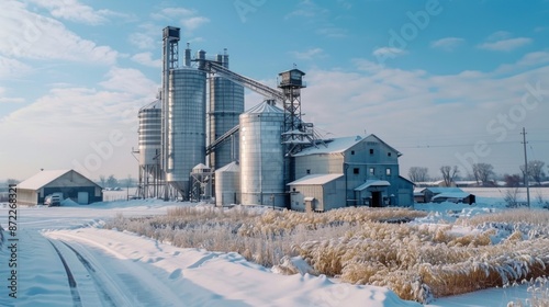 A snowy winter scene featuring a large grain silo complex situated on a rural landscape. A country road winds its way through the snow-covered fields photo