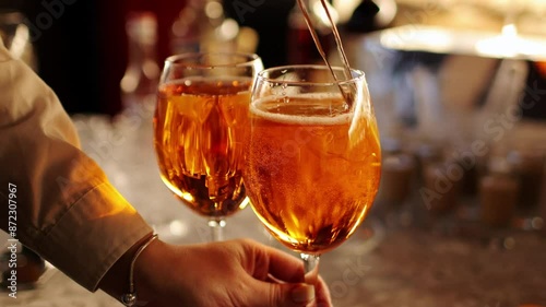 Bartender makes two glasses of cocktail Aperol spritz on bar counter, adds fresh orange slices. Typical alcoholic Italian beverage, aperitif made with Prosecco sparkling white wine and ice cubes