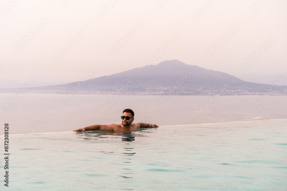 A man tourist enjoying or relaxing in a pool against mount vesuvius volcano in Campania Italy