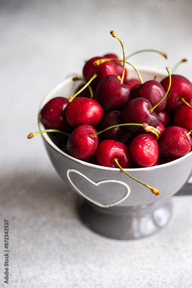 Fresh red cherries in a heart-decorated bowl on gray background Fresh red cherries in a heart-decorated bowl on gray background