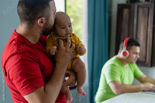 LGBT man kissing his son while his partner works