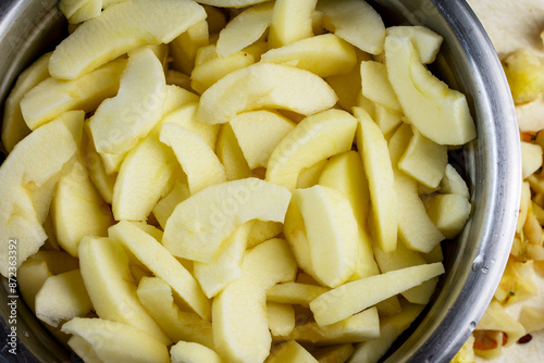 Close up view of gala apple slices in salt water in stainless bowl.  Preparation for a pie.  Scraps nearby.
