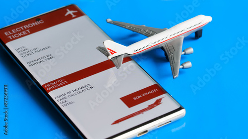 Electronic air ticket form on the screen of a mobile phone next to a toy passenger plane. Concept of buying online and using an electronic airline ticket for travel. Photo