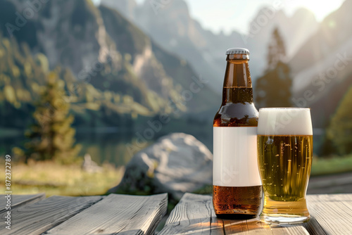 A close up of a bottle of beer with a blank mock up label on it and a glass of beer served together with brezels on the wooden table with a lake and mountains at sunset in the background photo