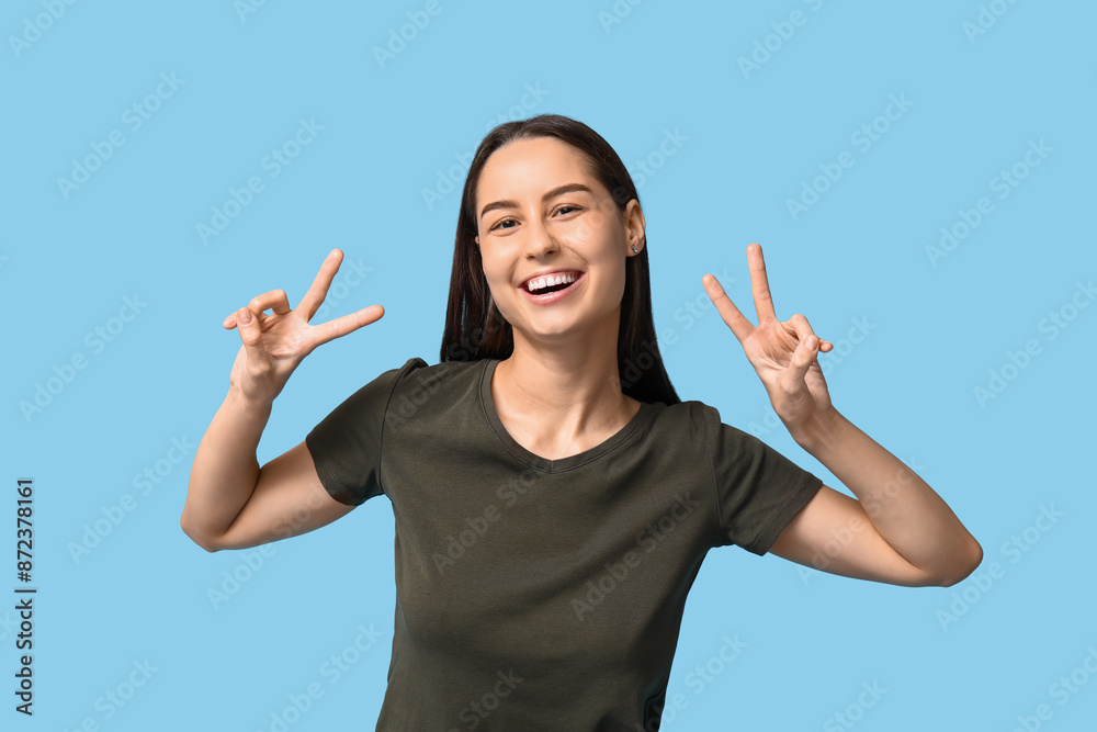 Beautiful young woman showing victory gesture on blue background Beautiful young woman showing victory gesture on blue background
