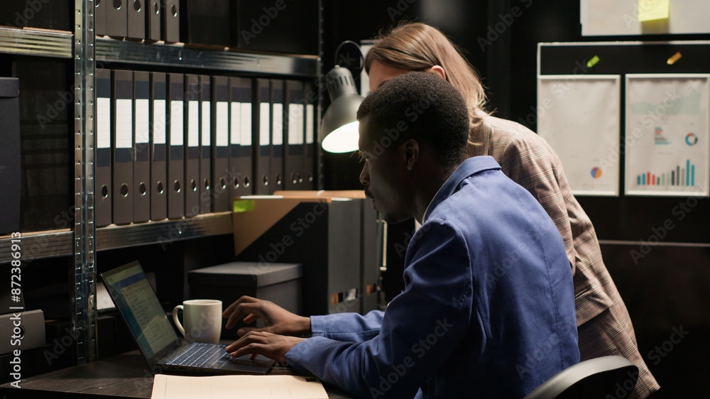 Caucasian and african american law enforcement personnel and investigators meticulously analyze evidence and exchange information in office. Black policeman and his female police partner review cases. Caucasian and african american law enforcement personnel and investigators meticulously analyze evidence and exchange information in office. Black policeman and his female police partner review cases.