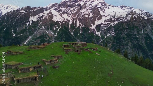 A lush green meadows with a village of homes made of wood. The village is surrounded by trees and the sky is cloudy at Chukail Banda, Swat Valley, Pakistan
