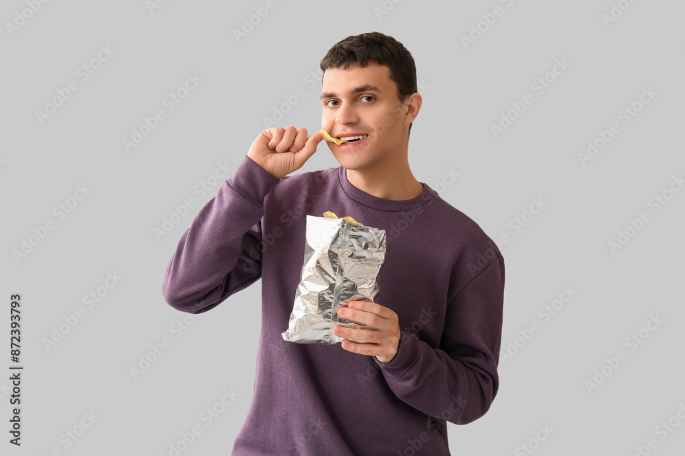 Young man eating potato chips on light background Young man eating potato chips on light background