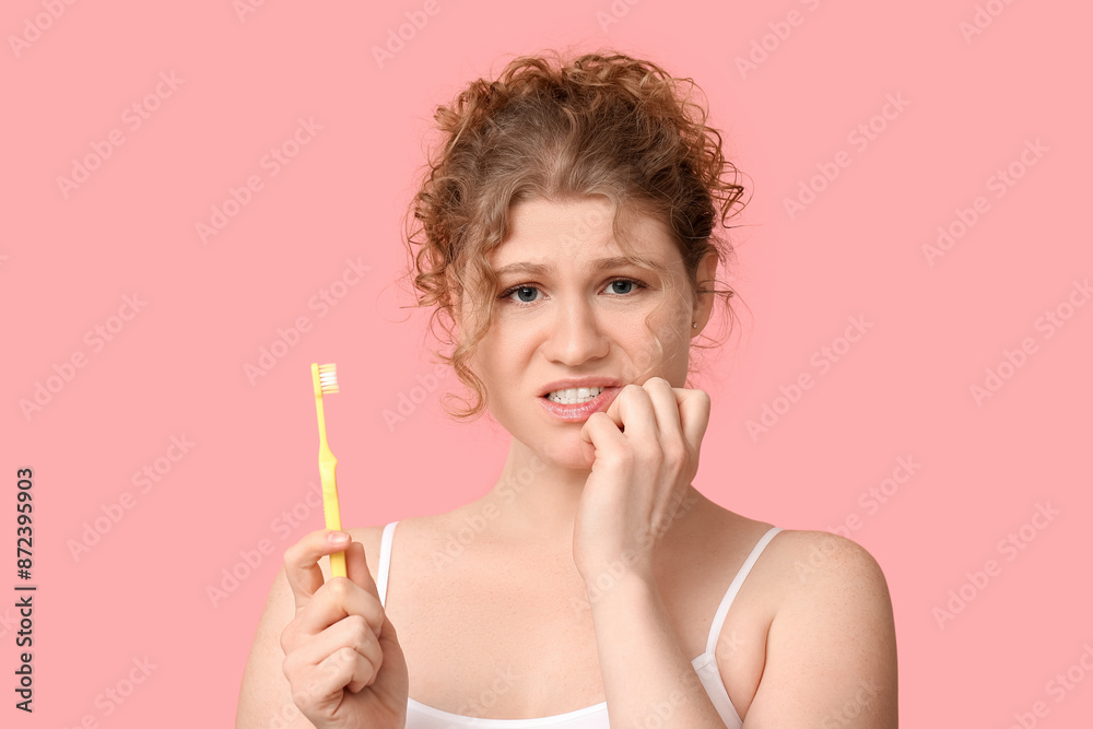 Beautiful young displeased woman with toothbrush on pink background Beautiful young displeased woman with toothbrush on pink background