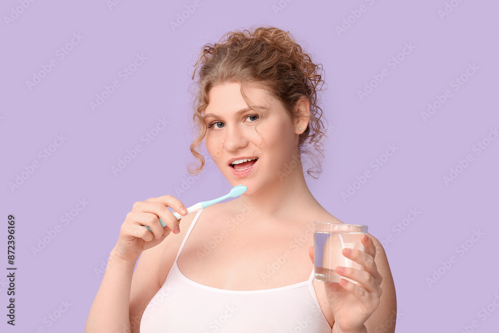 Beautiful young happy woman with glass of water brushing teeth on purple background Beautiful young happy woman with glass of water brushing teeth on purple background