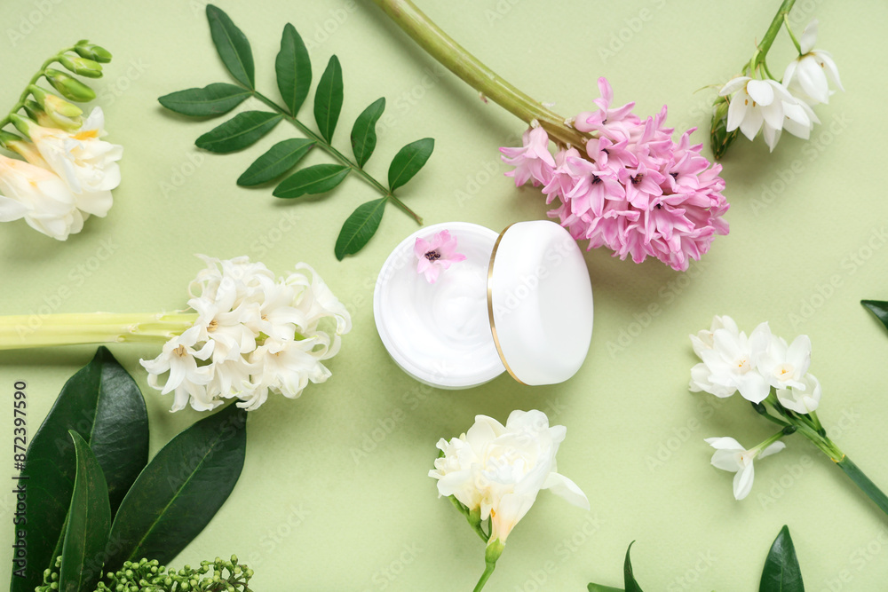 Composition with jar of cream and beautiful flowers on green background Composition with jar of cream and beautiful flowers on green background