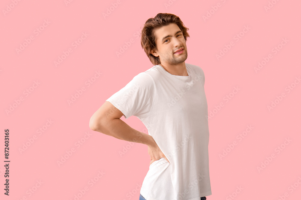 Handsome young man suffering from back pain on pink background Handsome young man suffering from back pain on pink background