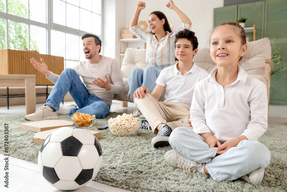 Cute little girl and her family watching football game with soccer ball at home