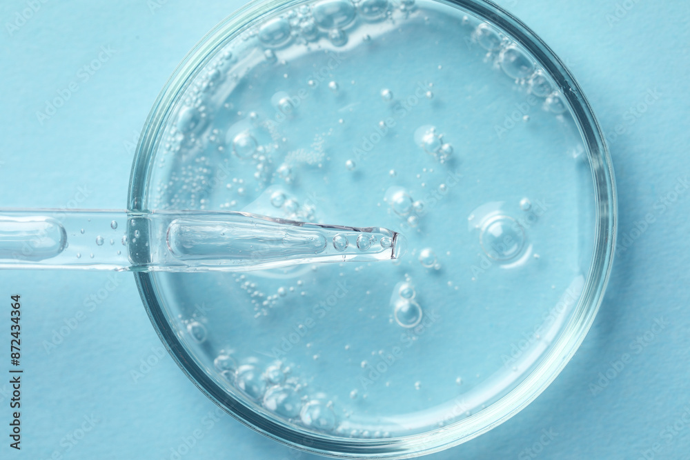 Glass pipette and petri dish with liquid on light blue background, top view Glass pipette and petri dish with liquid on light blue background, top view
