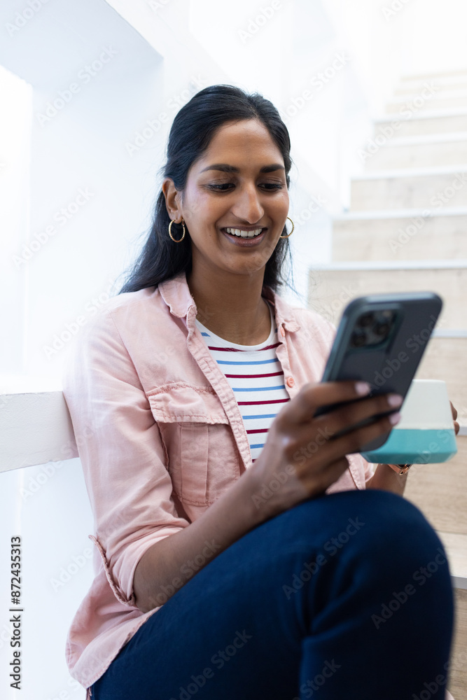Smiling woman sitting on stairs, using smartphone and holding coffee cup Smiling woman sitting on stairs, using smartphone and holding coffee cup