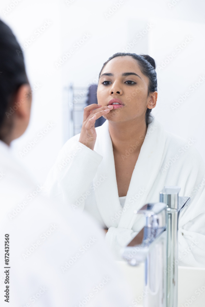 Applying lip balm, woman in white robe looking at mirror in spa bathroom Applying lip balm, woman in white robe looking at mirror in spa bathroom