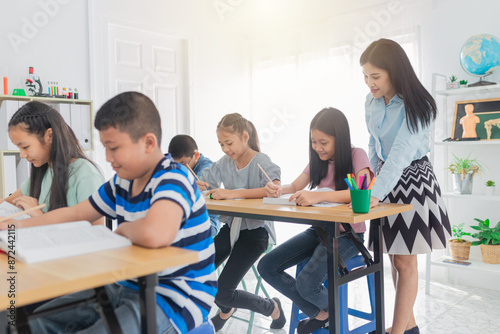 asian students group reading book and study with teacher in classroom, they sharing knowledge together, they explaining about important lesson to friends, happiness elementary school
