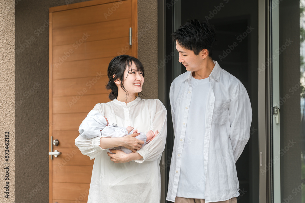 Fototapeta premium 新築のマイホーム・一軒家・一戸建ての玄関の前に立つ施主の夫婦と赤ちゃん・カップル・家族 