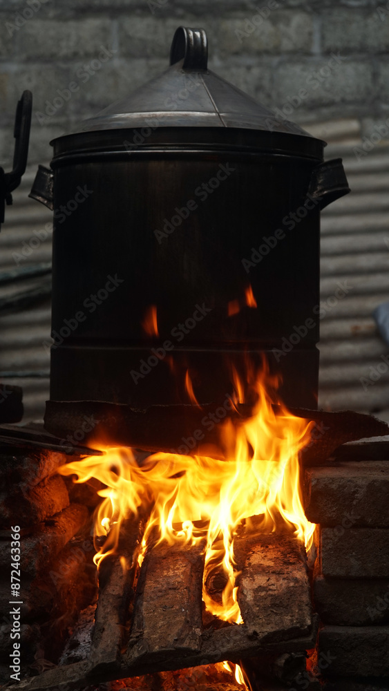 A fire burns in a wood burning stove with a black pot on top. Focus selected A fire burns in a wood burning stove with a black pot on top. Focus selected