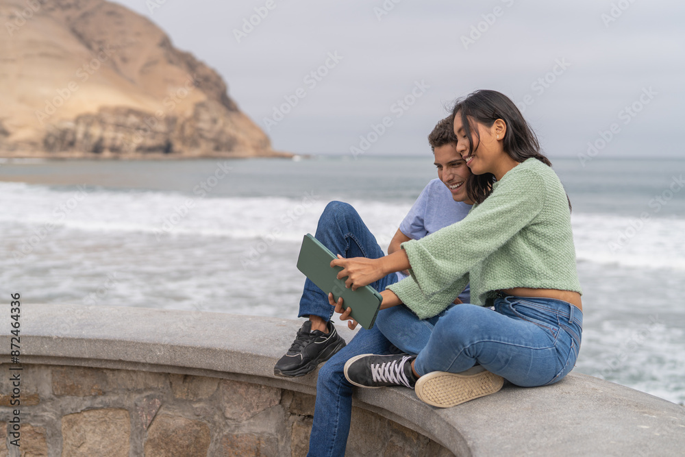 Fototapeta premium Couple taking selfie with digital tablet next to the sea