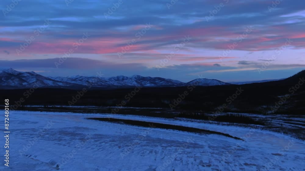 Aerial Zoom Out Idyllic Shot Of Bare Trees By Snowy Mountains Under Cloudy Sky During Tranquil Sunset - Calico Bluff, Alaska