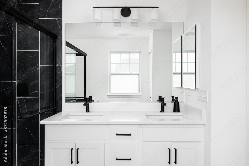 A white bathroom with a marble countertop, black faucets, and a shower with black marble tiles. A white bathroom with a marble countertop, black faucets, and a shower with black marble tiles.