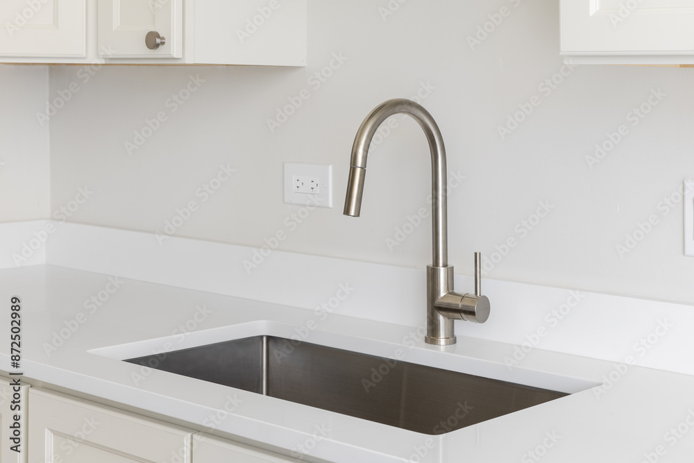 A kitchen sink detail with a polished chrome faucet, white marble countertop, and white cabinets. A kitchen sink detail with a polished chrome faucet, white marble countertop, and white cabinets.